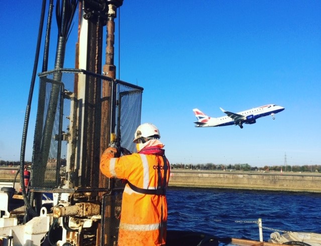 Site operative carrying out over water work as a plane fly's by in the background